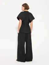 Pantalón negro de lanita viscosa, corte wide leg con gran caída y movimiento. Acceso mediante cierre metálico, gancho pantalonero y botón interno. Incluye lazo en cintura con media caña marcaria de níquel.