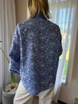 Camisa de manga larga con diseño de flores bordadas en color blanco sobre base azul. Presenta cuello clásico, cierre frontal con botones y mangas abullonadas con puños elásticos.