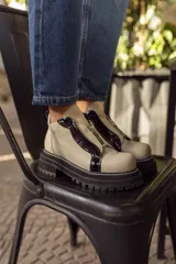 Borcego de cuero con punta redonda, diseño bicolor en beige y negro, con cierre frontal y suela track de goma negra.