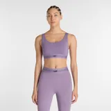 Top deportivo New Balance de impacto moderado, color lila, con cuello redondo y banda elástica inferior con logo de la marca. Confeccionado en tejido técnico de alto rendimiento con copas extraíbles.