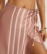 Salida de playa tipo pollera traspasada con lazo, de tejido satinado con estampado de rayas horizontales en el ruedo.