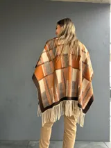 Ruana abierta con diseño de cuadros en tonos tierra, naranja y beige, con terminación de flecos en el ruedo.