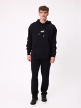 Canguro marrón con capucha y bolsillo frontal, con un diseño gráfico colorido en la espalda que representa una casa surrealista con el texto 'Supreal State of Mind'.