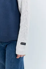 Cardigan de punto con diseño bicolor, cuerpo en color marrón y mangas largas en color crema con textura trenzada. Presenta cuello polo, cierre frontal con cremallera y puños acanalados.