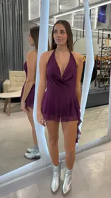 Vestido corto color morado con diseño de cuello halter, escote en V pronunciado con caída drapeada y falda fluida con capas de tela traslúcida que incluye un short interior.