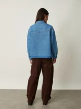 Camisa de denim celeste oversize con bolsillos frontales, cierre de botones metálicos y detalles de tachas en el cuello y la parte delantera.