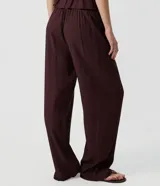 Pantalón palazzo de viscosa texturizada color marrón, de tiro alto con cintura elástica, lazo frontal regulable y bolsillos laterales.