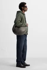 Bolso de hombro tipo media luna, fabricado en piel craquelada color marrón oscuro. Tiene un compartimento principal con cierre de cremallera y un bolsillo interior también con cremallera.