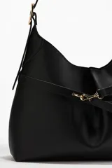 Cartera tipo hobo de diseño slouchy en color negro, confeccionada en material texturizado. Presenta una correa de hombro ajustable y un detalle de tira fina frontal con cierre de mosquetón metálico dorado que frunce el centro de la pieza. Cuenta con cierre magnético oculto y forro interior.