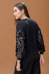 Sweater negro de cuello redondo con mangas largas decoradas con lentejuelas brillantes del mismo tono. Presenta puños y ruedo acanalados, con un corte relajado y cómodo.