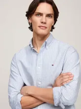 Camisa de corte regular confeccionada en algodón Oxford, con diseño de rayas verticales en tonos blanco y azul. Presenta cuello con botones, puños redondeados y logo de la marca bordado en el pecho.