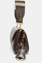 Bolso alargado color marrón con pespuntes en contraste. Tiene un bolsillo exterior con botón imantado, doble asa bandolera ajustable (una de tela), compartimento interior con cremallera y cierre con solapa y clip metálico.