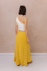 Falda larga envolvente de color mostaza, con diseño asimétrico, lazo ajustable en la cintura y volados en cascada.