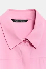 Camisa azul de manga corta y cuello solapa con costura horizontal en el pecho y cierre frontal oculto con botones.