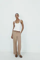 Pantalón de tiro alto color marrón, de corte recto y holgado, con bajo acabado en vuelta. Incluye bolsillos delanteros y cinturón fino a contraste con hebilla metálica.