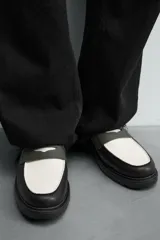 Mocasín de cuero marrón oscuro con antifaz en tono camel. Presenta horma redonda y suela track gruesa de goma negra.