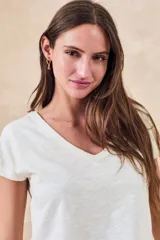 Remera blanca de algodón con escote en V y mangas cortas. Presenta un diseño estampado o bordado en negro de estilo tribal o geométrico en los laterales y mangas.