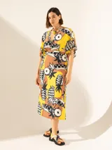 Vestido midi con estampado de piñas y motivos geométricos en tonos amarillo, marrón y negro. Presenta escote en V, mangas cortas y corte en la cintura con aberturas laterales.