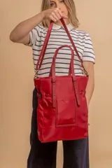 Bolso tipo tote bag de símil cuero color rosa pálido, con asas dobles y detalles de costura en color beige claro. Presenta un bolsillo frontal rectangular aplicado y herrajes metálicos.