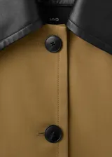Chaqueta de corte amplio en tono tostado, con solapas y cuello de cuero sintético en color negro kontrastante. Posee cierre frontal de botones oscuros y bolsillos laterales discretos.