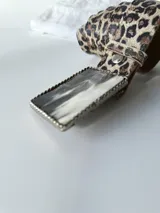 Cinto de cuero con estampado animal print y hebilla rectangular con diseño abstracto en blanco y negro.