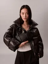 Cartera estructurada Calvin Klein de piel sintética negra, con diseño de asas superiores y bolsillos laterales. Cuenta con cierre de cremallera y logo metálico grabado en la parte delantera.