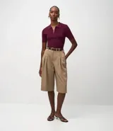 Blusa polo de punto color mostaza, ajustada al cuerpo, con cuello y manga corta. Presenta una cremallera frontal que llega hasta el escote.