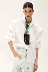 Camisa blanca de poplin con cuello clásico, mangas largas abullonadas y cierre frontal con botones. Presenta un bordado con forma de boca en el frente.