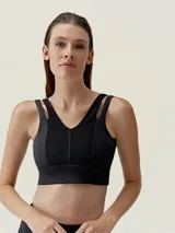 Top deportivo negro de sujeción media-alta, con escote en V y tirantes dobles en los hombros. Presenta paneles centrales con textura acanalada y una banda ancha inferior.