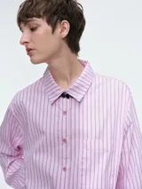 Camisa oversize de popelina de algodón con diseño de rayas verticales, cuello clásico, cierre frontal con botones, manga larga con puños anchos y bolsillo aplicado en el pecho.