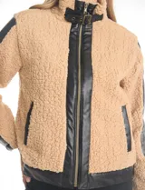 Campera de corderito sintético color beige con paneles y detalles en cuero sintético negro. Presenta cuello alto con tira y hebilla metálica, cierre frontal metálico y mangas largas con paneles de cuero sintético.
