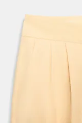Bermudas color amarillo claro de tiro alto con bolsillos laterales ocultos en costura, detalle de pinzas en delantero y cierre frontal con cremallera y ganchos metálicos.