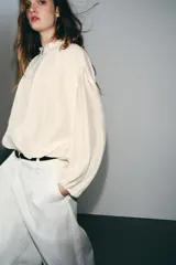 Chaqueta bomber de cuello subido y manga larga, con acabado satinado en color beige. Presenta pliegues frontales, bolsillos laterales ocultos en costura y cierres elásticos en puños y cintura. Cierre frontal con cremallera.