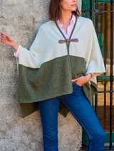 Ruana de tejido de punto con diseño bicolor en tonos crudo y verde oliva, con cierre frontal mediante hebilla de cuero.