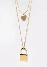 Collar doble dorado con cadena fina, un dije circular y un dije con forma de candado.