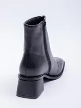 Botín negro de cuero sintético, caña corta, con punta cuadrada y cierre frontal central. Posee un taco bajo y grueso.