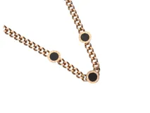 Collar de acero inoxidable con baño de oro rosa y cadena de eslabones. Incluye tres dijes circulares con centro de ónix negro y números romanos grabados en el borde.