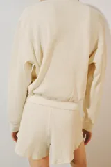 Jersey de punto waffle de algodón color beige, con cuello redondo, cierre frontal parcial con botones en contraste y manga larga con puños elásticos.