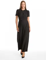 Enterito de seda fría color negro, con cuello a la base fruncido, escote en V con botones metálicos y detalle plisado vertical en el frente. Presenta mangas cortas con terminación fruncida, cintura con lazo de ajuste y pantalón de pierna ancha con caída fluida.