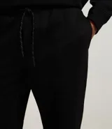 Pantalón jogger negro de algodón y poliéster, con cintura elástica y cordón ajustable. Presenta bolsillos laterales y puños ajustados en los tobillos.