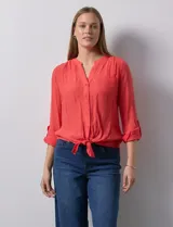 Blusa blanca de gasa marca Zac & Rachel, con cuello a la base, escote en V, abertura central con botones, bolsillo aplicado en el pecho y mangas largas regulables con presilla y botón. Tiene terminación opcional de nudo en el ruedo.