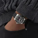 Reloj analógico Guess con caja de acero inoxidable, esfera negra con índices luminiscentes y segundero rojo, y malla de silicona negra.