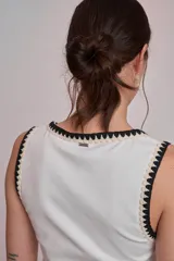 Remera negra sin mangas, tipo musculosa, con escote redondo y ribetes blancos con apliques de perlas en el contorno del cuello y las sisas.
