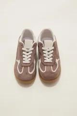 Zapatilla urbana de gamuza color marrón con detalles en beige, cordones claros y suela de goma tipo caramelo.