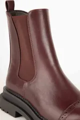 Bota Chelsea de cuero sintético color negro, con elástico lateral, puntera redondeada con detalle de perforaciones y suela track.