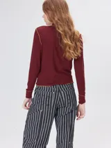 Polera de manga larga confeccionada en tela rib color bordó, con cuello alto y hombreras. Presenta costuras a la vista con pespuntes en hilo de color contrastante en el cuello, puños, hombros y ruedo.