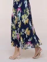 Vestido midi azul marino con estampado floral multicolor, confeccionado en gasa liviana con falda plisada. Tiene escote en V, mangas cortas estilo mariposa y lazo ajustable en la cintura.