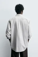 Camisa de corte regular fit confeccionada en tejido de algodón con estampado de cuadros pequeños. Presenta cuello abotonado, manga larga con puños abotonados, bolsillo plastrón en el pecho y cierre frontal con botones.