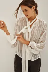 Camisa de transparencia con diseño a rayas verticales, cuello con lazo integrado y mangas largas abullonadas con puños ajustados.
