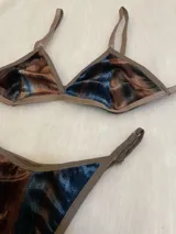 Conjunto de lencería compuesto por un bralette de corte triangular y una tanga regulable. Ambas piezas están confeccionadas en terciopelo con un estampado abstracto en tonos azul, marrón y negro, con terminaciones en ribete color marrón.